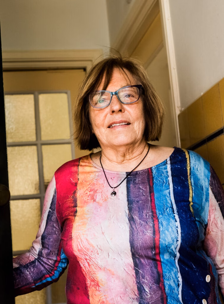 Portret van oudere vrouw met bril en kleurrijke blouse.
